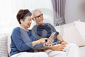 Senior Asian couple grandparents using a smart phone together on sofa at home.