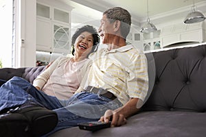 Senior Asian Couple At Home On Sofa Watching TV Together