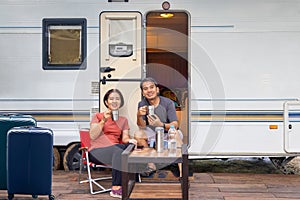 Senior asian couple joyful and relax sitting in front of caravan home on vacation