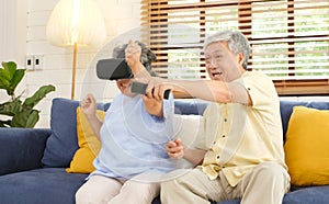 Senior asian couple playing virtual reality headset and using digital tablet in home living room with happiness emotion,