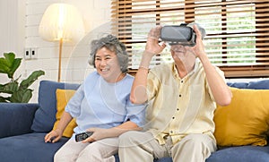 Senior asian couple playing virtual reality headset and using digital tablet in home living room with happiness emotion,