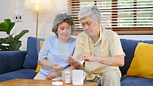 Senior asian couple take pill medicine for elderly healthy lifestyle while sitting on sofa at home living room, retirement people