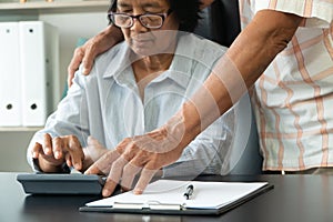 Senior Asian couple using the calculator and paperwork on desk at home to calculate expenses and income. And savings after