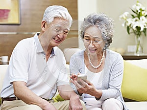 Senior asian couple using cellphone at home