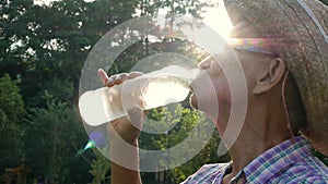 Senior Asian farmer drinking some water from bottle in the garden.