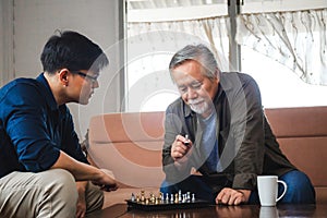 Senior asian father and middle aged son playing chess game in living room, Happiness Asian family concepts