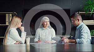 Senior Asian female mentor talking to younger colleagues interns in office.