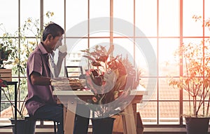 Senior Asian man having morning coffee while reading newspaper in his houseplant garden at home