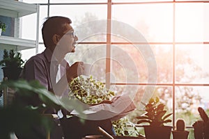 Senior Asian man having morning coffee while reading newspaper in his houseplant garden at home