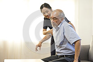 Senior asian man holding caregivers hand and getting up from the sofa while staying at the nursing home.