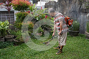 Senior asian man mowing grass at his own home garden