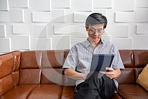 Senior Asian man playing tablet on sofa in living room at home  Portrait of Asian elderly man is Relaxing and Happiness With