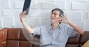 Senior Asian man playing tablet and video call on sofa in living room at home  Portrait of Asian elderly man is Relaxing and