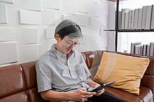 Senior Asian man playing tablet and video call on sofa in living room at home  Portrait of Asian elderly man is Relaxing and