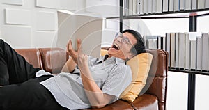 Senior Asian man reading book and Laughing on sofa in living room at home  Portrait of Asian elderly man is Relaxing and Happiness