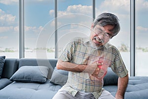 Senior Asian man sitting on couch and using hand touch to chest from having heart attack in living room at home