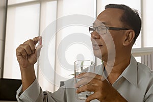 Senior asian man taking red pills with water glass.