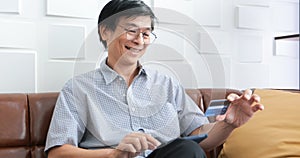 Senior Asian man using smart phone shopping online and paying with credit card at home