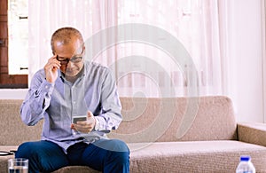 Senior asian man wearing glasses and using cell phone at home,Relax time,Senior lifestyle concept,Long sighted