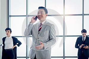 Senior Asian smiling businessman boss in suit talking on mobile phone and laughing at the window office workplace with