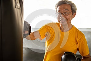 Senior asian sport man in  boxing gloves punching bag  in fitness gym . elder male exercising , workout, training ,healthy ,