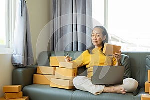 Senior Asian woman doing online shopping at home with boxes and laptop