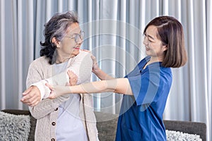 Senior Asian woman got medical service visit from caregiver nurse at home while doing physical therapy to shoulder stretching for