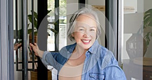 Senior Asian woman with grey hair smiles warmly, wearing a denim shirt