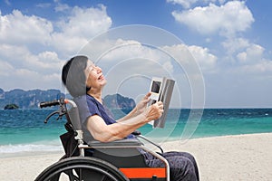 Senior asian woman laughing while reading magazine on beach