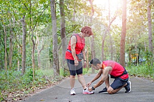 Senior asian woman with man or personal trainer tying shoe laces in the park