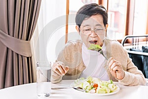 Senior Asian woman patient eating fresh and clean vegetarian salad lettuce, tomato and sliced radish served by a nurse at home.