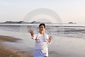 Senior asian woman practicing Tai Chi exercise during sunset at the beach