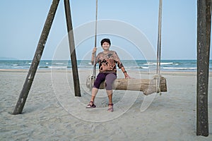 Senior Asian woman relaxing on a wood plank swing on the beach