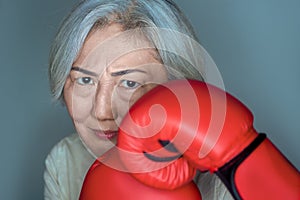 senior asian woman standing in a fighting pose with red boxing gloves on blue background. Feminism, women power concept