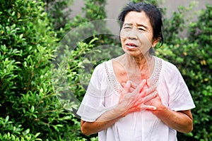 Senior Asian woman suffering from heartburn, chest pain, difficult to breathe standing outdoor