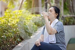 Senior athletic woman drinks water from a bottle after running in the park