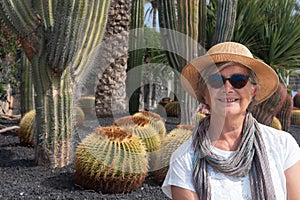 A senior attractive woman with straw hat sitting in the garden with cactus plants around her