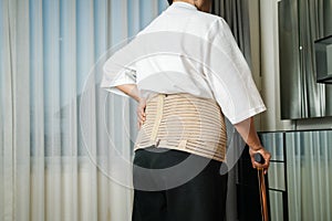 Senior back pain woman with walking stick at home