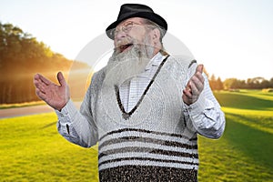 Senior beaded man is laughing out loud on green meadow background.