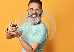 Senior bearded man with glasses holds a glass of water and looks away in disbelief.