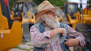 Senior bearded man looking around at new tractors picking business card from pocket and looking at camera. Portrait of