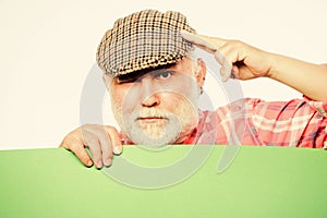 Senior bearded man peek out of banner place announcement. Pensioner grandfather in vintage hat hold poster information