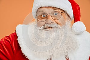 Senior bearded man in red Santa costume looking at camera