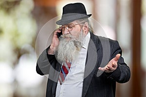 Senior bearded salesman or businessman negotiating on phone standing on abstract bokeh background.