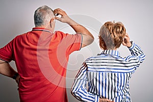 Senior beautiful couple standing together over isolated white background Backwards thinking about doubt with hand on head
