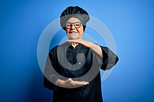 Senior beautiful grey-haired chef woman wearing cooker uniform and hat over blue background gesturing with hands showing big and