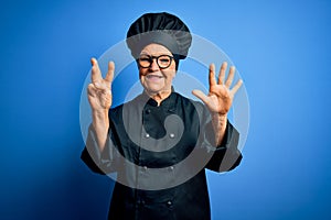 Senior beautiful grey-haired chef woman wearing cooker uniform and hat over blue background showing and pointing up with fingers