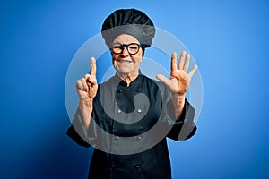 Senior beautiful grey-haired chef woman wearing cooker uniform and hat over blue background showing and pointing up with fingers