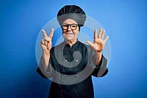 Senior beautiful grey-haired chef woman wearing cooker uniform and hat over blue background showing and pointing up with fingers