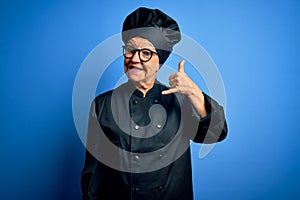 Senior beautiful grey-haired chef woman wearing cooker uniform and hat over blue background smiling doing phone gesture with hand